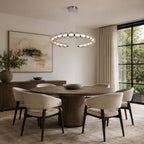 A Clérachic pendant ring over a round wooden dining table with four cream chairs, beside a tall black-framed window.