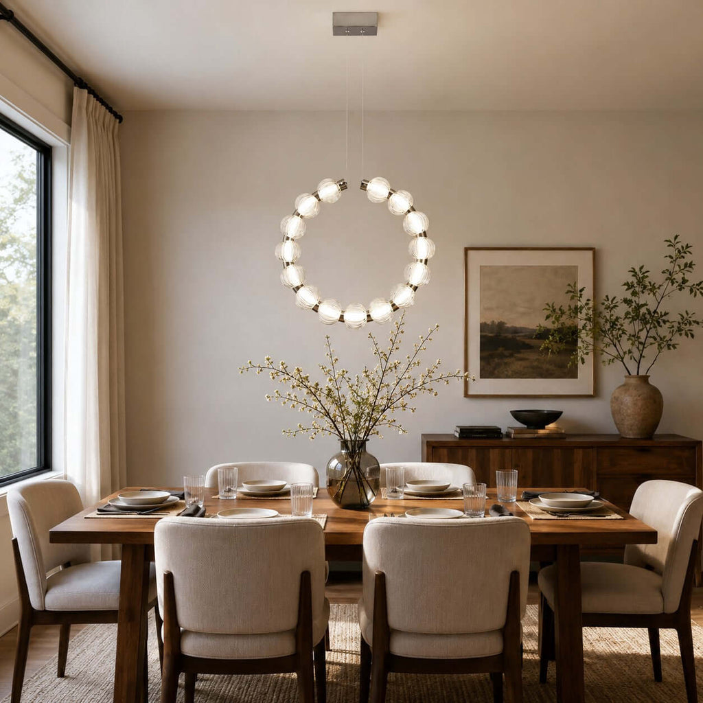 Hung vertically as a full circle of glowing glass beads, this Clérachic pendant sits over a set wooden dining table.