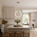 A circular Clérachic pendant glows over a white island with three woven stools in a bright cream kitchen.
