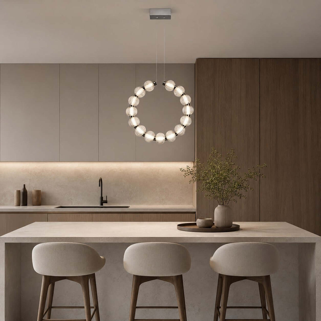 The ring of this Clérachic pendant hangs vertically in front of grey cabinets, above an island with three rounded stools.