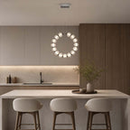 The ring of this Clérachic pendant hangs vertically in front of grey cabinets, above an island with three rounded stools.