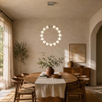 A Clérachic pendant circle hangs vertically above an oval wooden table with a linen runner, in a room with sheer curtains.