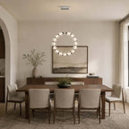 A glowing circle of glass beads, this Clérachic pendant hangs vertically over a dining table with cream chairs and a landscape print.