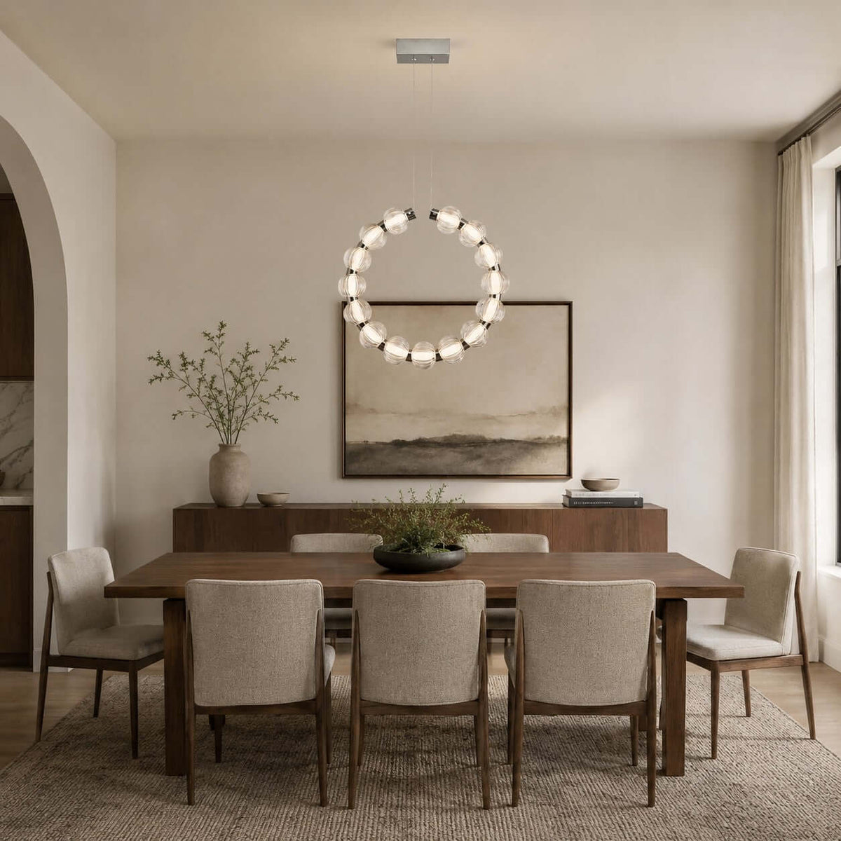 A glowing circle of glass beads, this Clérachic pendant hangs vertically over a dining table with cream chairs and a landscape print.