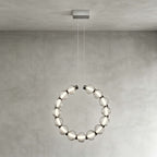 A Clérachic pendant hung vertically from a rectangular canopy, its ring of lit glass beads against a grey wall.