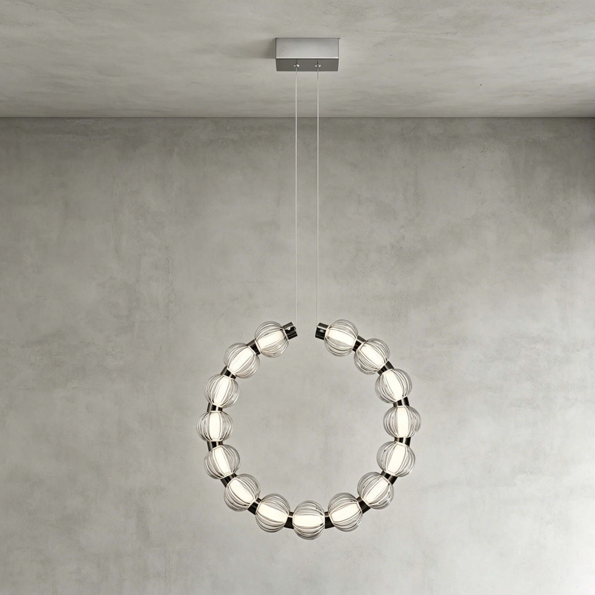 A Clérachic pendant hung vertically from a rectangular canopy, its ring of lit glass beads against a grey wall.