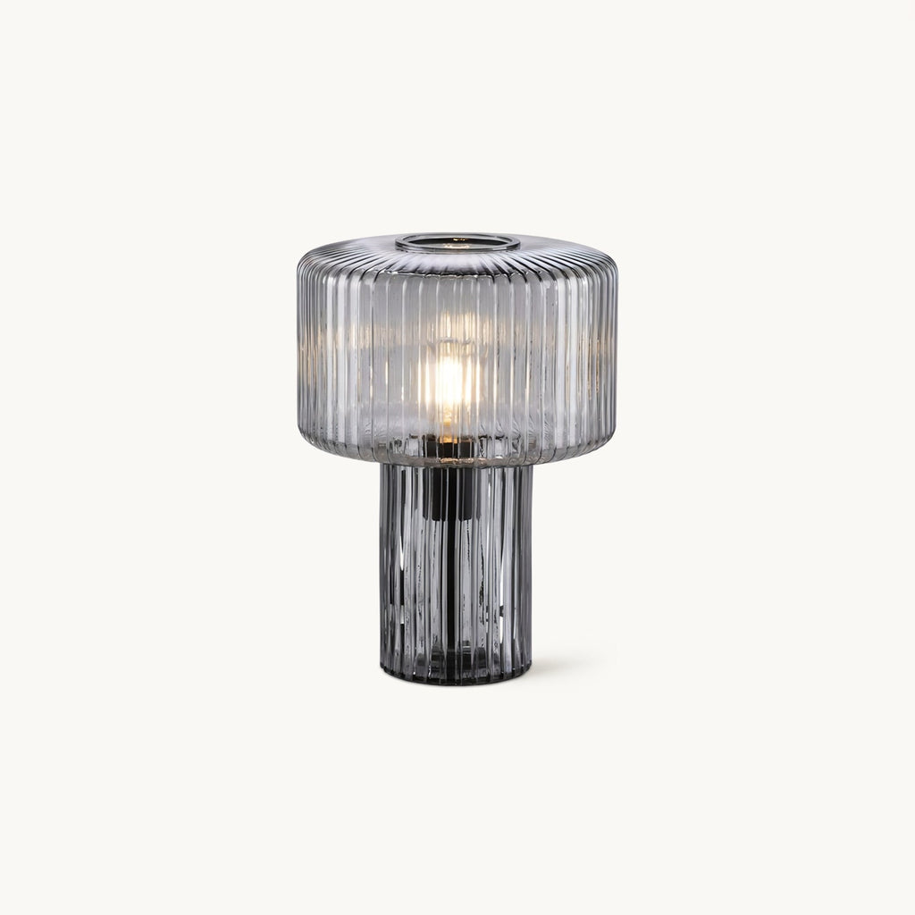 A ribbed smoky grey glass Clérachic table lamp with a wide drum shade over a slim fluted base, lit, on a plain white backdrop.