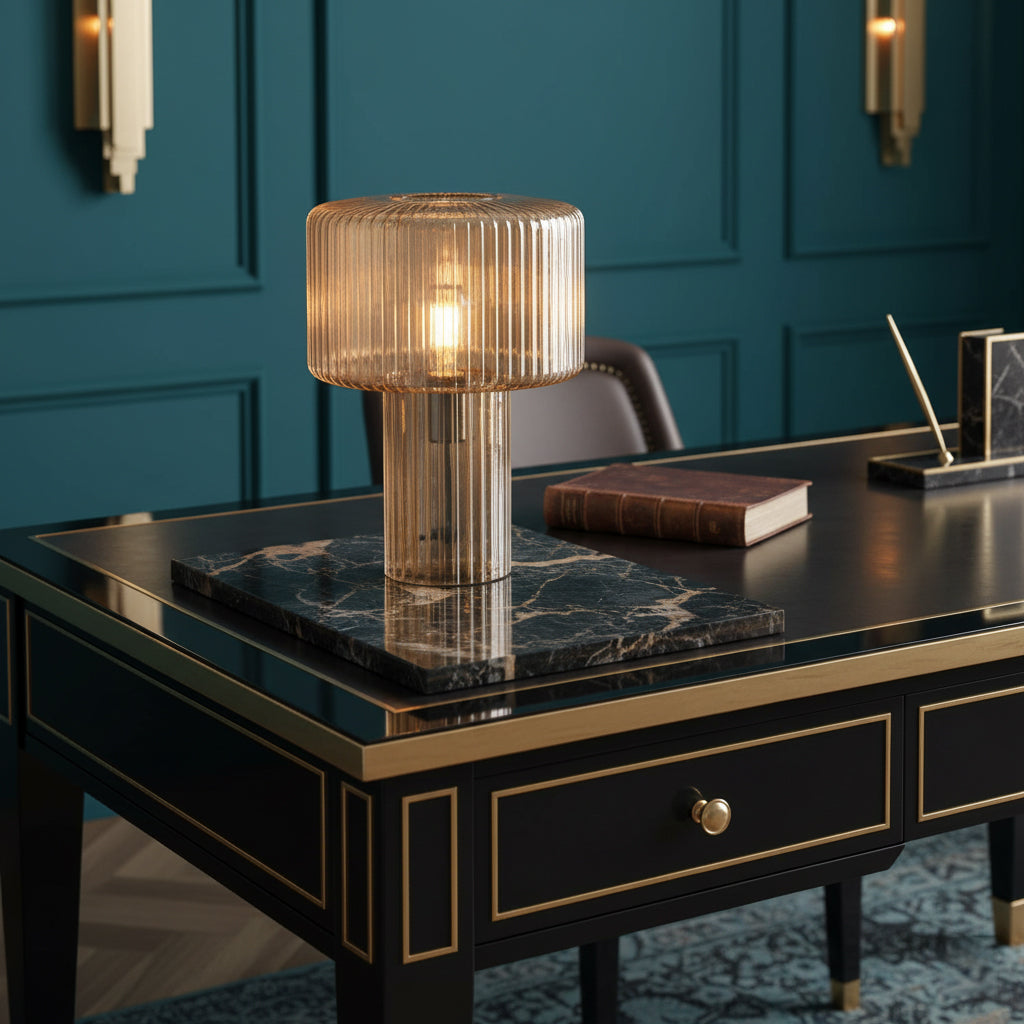 Cognac ribbed glass Clérachic lamp on a black desk with brass trim, standing on a marble tray beside a book, against teal panelling.