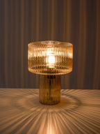 Cognac ribbed glass Clérachic lamp glowing on a tabletop, casting a starburst of light onto the surface and a curtain behind.