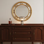 A small ribbed glass Clérachic table lamp on a dark wood sideboard, with a round gold mirror above and a whisky decanter beside it.