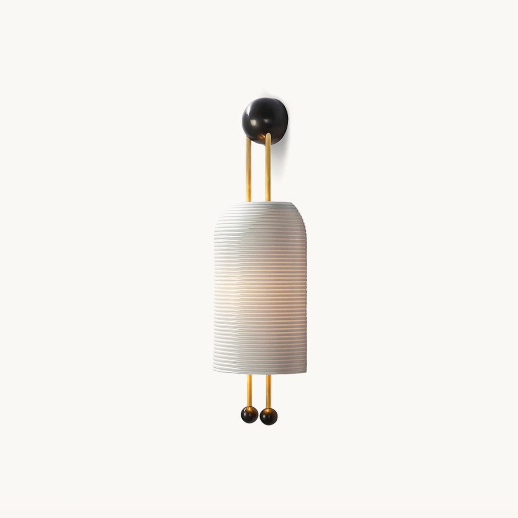 Ribbed white cylindrical shade on gold-finish rods with a black round wall plate and two black ball ends, this Clérachic wall light on white.