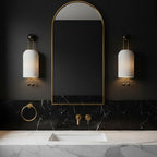 Pair of Clérachic ribbed wall lights flanking a tall arched mirror above a black marble backsplash and white marble basin top.