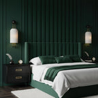 Two Clérachic wall lights with ribbed white shades either side of a dark green velvet bed, with black bedside tables and gold handles.