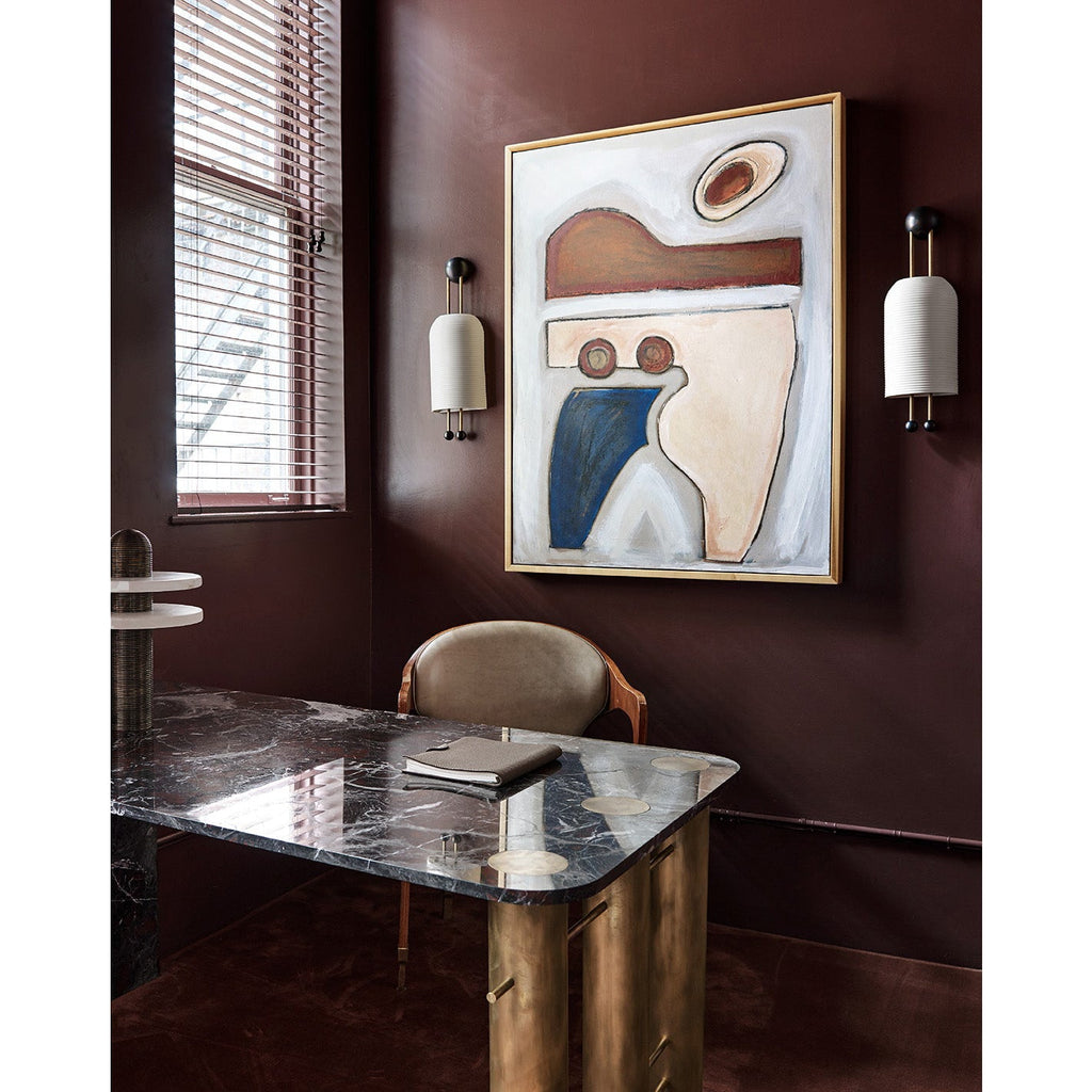 Clérachic wall light with a ribbed white shade on a deep burgundy wall, with a large abstract painting and a black marble desk below.