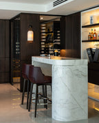 This Clérachic ribbed wall light glowing on a dark panelled wall above a white marble bar counter with two burgundy bar stools.