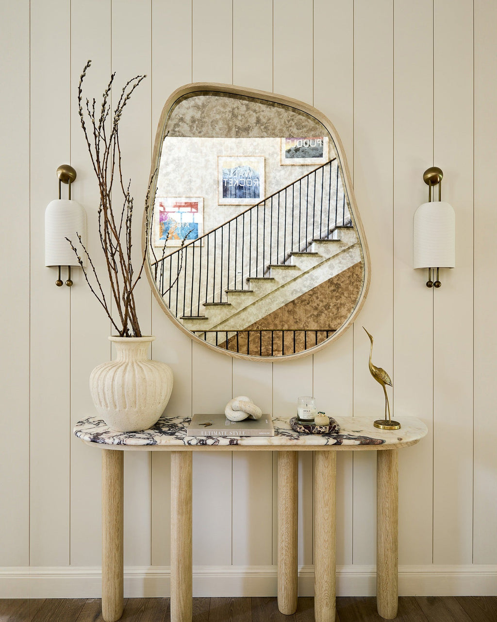 Pair of Clérachic ribbed wall lights either side of a curved-edge mirror above a marble-top console with a vase of bare branches.