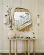 Pair of Clérachic ribbed wall lights either side of a curved-edge mirror above a marble-top console with a vase of bare branches.
