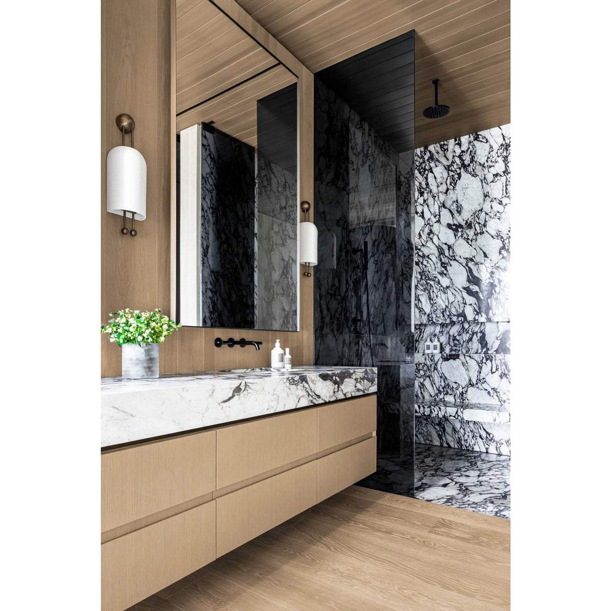 Ribbed white Clérachic wall light on a wood-clad wall by a floating oak vanity with a marble top and a dark marble shower beyond.