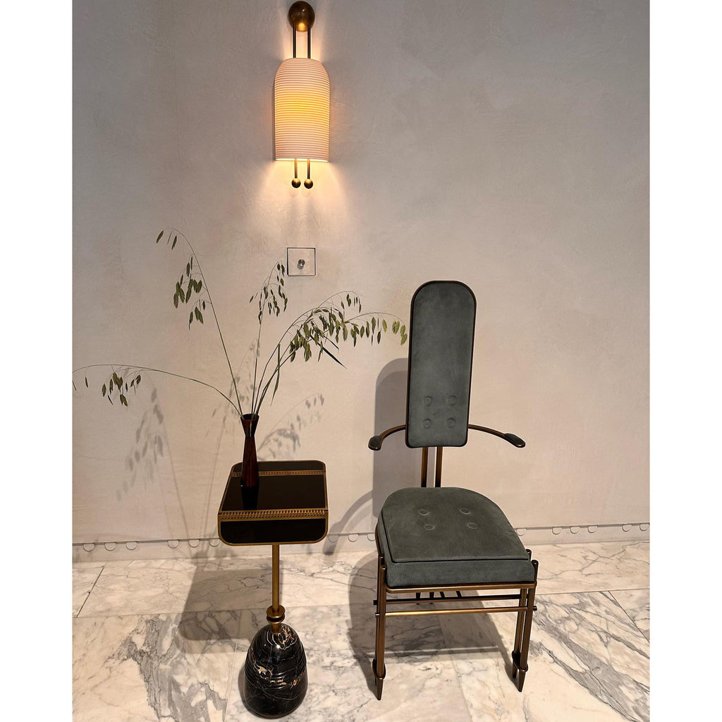 Lit Clérachic ribbed wall light above a dark green velvet chair and side table with eucalyptus stems, against a pale plaster wall.