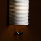 Close view of the horizontal ribbing on the lower shade and the two gold rods ending in black balls on this Clérachic wall light.