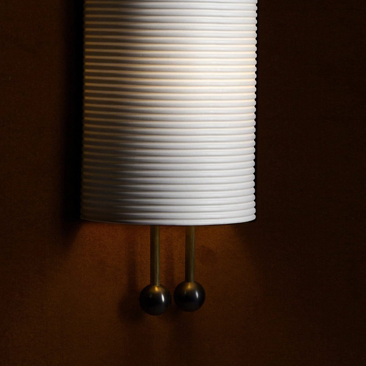 Close view of the horizontal ribbing on the lower shade and the two gold rods ending in black balls on this Clérachic wall light.