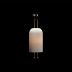 This Clérachic ribbed wall light, softly lit and set against a plain black backdrop, with its black wall plate and gold rods above the shade.