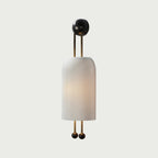 Clérachic wall light with a ribbed white shade and gold rods, lit softly and photographed against a pale grey-white wall.