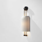 A lit Clérachic ribbed wall light casting a gentle shadow on a bright white wall, with a black wall plate and black ball ends.