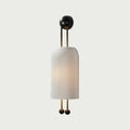 A Clérachic wall light with a ribbed white shade glowing faintly, set on a light grey-green backdrop with gold rods and black ball ends.