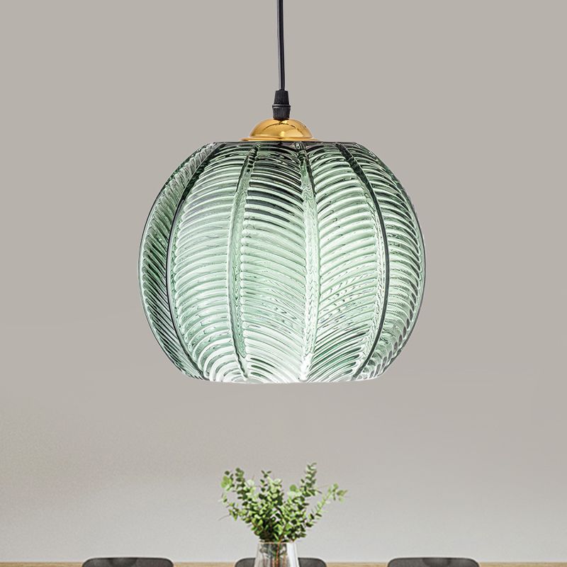 Clérachic Ribbed Green Glass Pendant Light hung above a dining table, its leaf-vein ribbed globe capped in gold-tone metal against a grey wall.