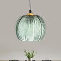 Clérachic Ribbed Green Glass Pendant Light hung above a dining table, its leaf-vein ribbed globe capped in gold-tone metal against a grey wall.