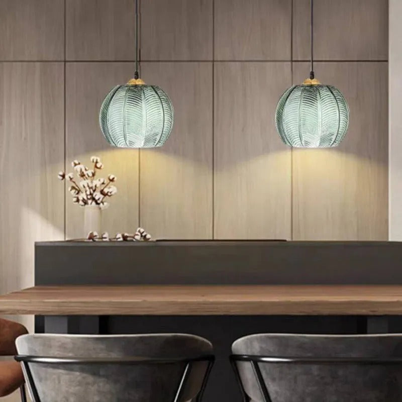 A pair of Clérachic Ribbed Green Glass Pendant Lights lit above a kitchen island, washing warm striped light down the wood-panelled wall.