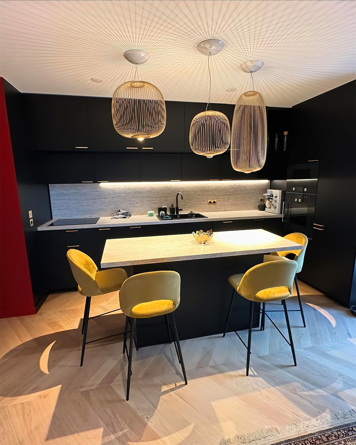 Three Clérachic wire-cage pendants in a copper tone hang over a kitchen island with yellow velvet stools and a herringbone floor.