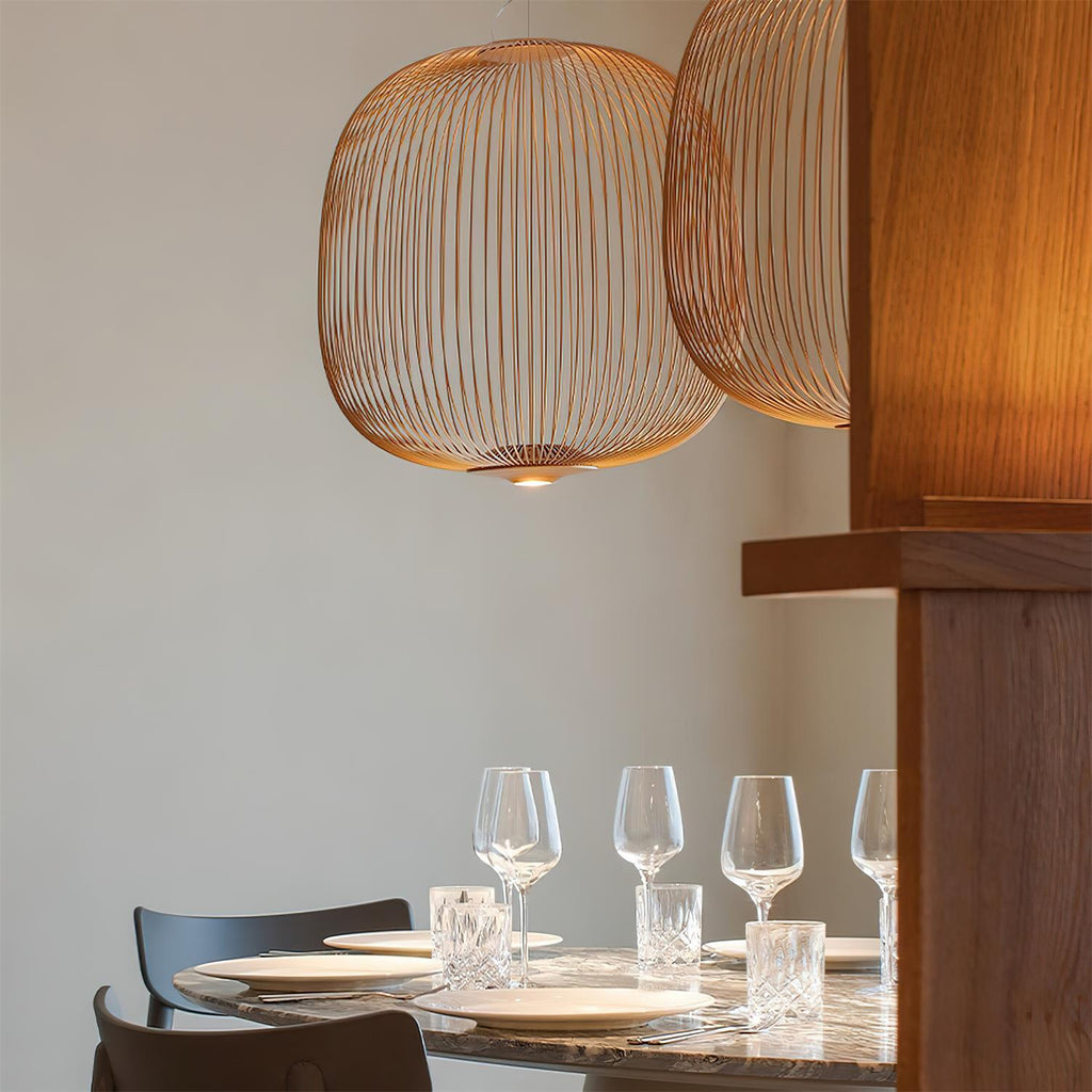 Close view of a copper-toned Clérachic wire-cage pendant above a set dining table with wine glasses and white plates.