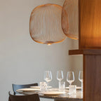 Close view of a copper-toned Clérachic wire-cage pendant above a set dining table with wine glasses and white plates.