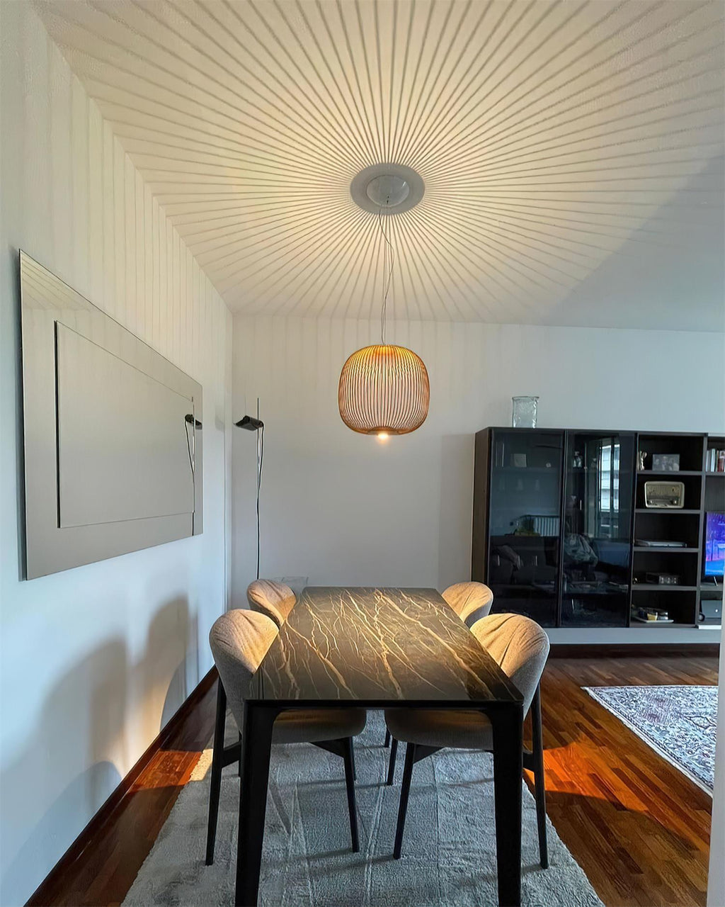 A small copper-toned Clérachic wire-cage pendant hangs over a dark dining table, with a ceiling canopy and fine wires fanning out above.