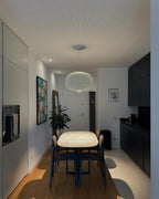 A white wire-cage Clérachic pendant hangs over a long marble-topped dining table in a narrow kitchen and dining room.