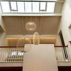Two white wire-cage Clérachic pendants hang at different heights in a high space with a skylight and a white balustrade.