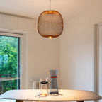 A copper-toned round Clérachic wire-cage pendant glows in a pale room beside a glass door, above a table with two glass carafes.