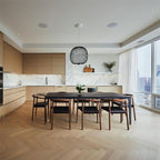 A small black wire-cage Clérachic pendant hangs over a long dark dining table in a bright kitchen with a herringbone floor.