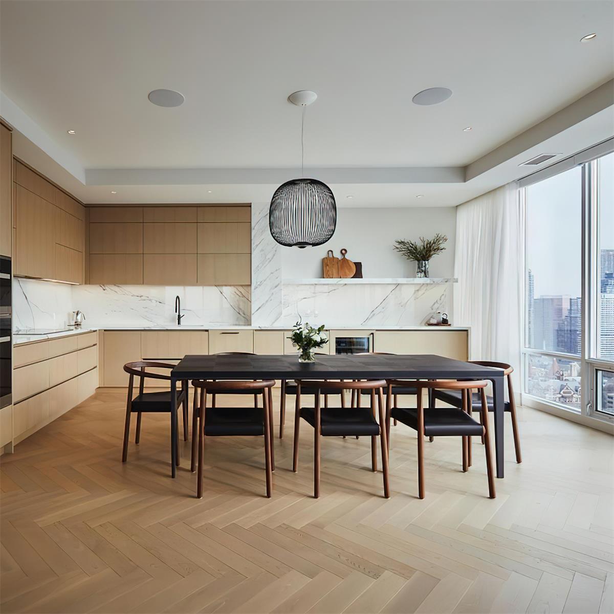 A small black wire-cage Clérachic pendant hangs over a long dark dining table in a bright kitchen with a herringbone floor.