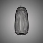 The tall oval wire-cage Clérachic pendant in black, with its fine wires and a lit base against a grey backdrop.