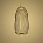 The tall oval wire-cage Clérachic pendant in a gold finish against a warm yellow backdrop.