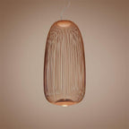 The tall oval wire-cage Clérachic pendant in a copper finish, glowing against a muted pink-brown backdrop.