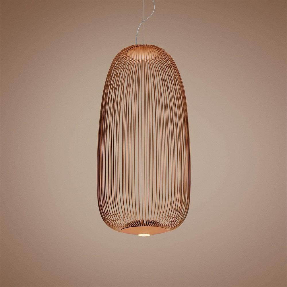 The tall oval wire-cage Clérachic pendant in a copper finish, glowing against a muted pink-brown backdrop.