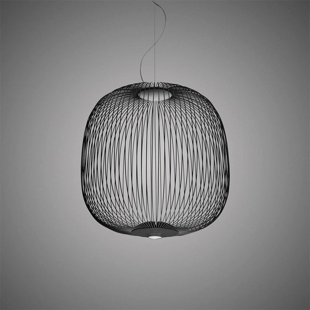 The wide, rounded wire-cage Clérachic pendant in black against a grey backdrop, with a lit base underneath.