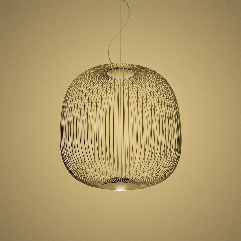 The wide, rounded wire-cage Clérachic pendant in a gold finish against a warm yellow backdrop.