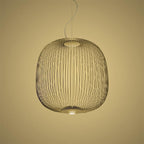 The wide, rounded wire-cage Clérachic pendant in a gold finish against a warm yellow backdrop.