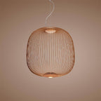 The wide, rounded wire-cage Clérachic pendant in a copper finish against a soft pink-brown backdrop.