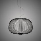 The low, wide drum-shaped wire-cage Clérachic pendant in black, with its curling cord above, on a dark grey backdrop.